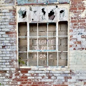 Image of an old building with broken windows where someone has scrawled 'Home Sweet Home' in chalk.